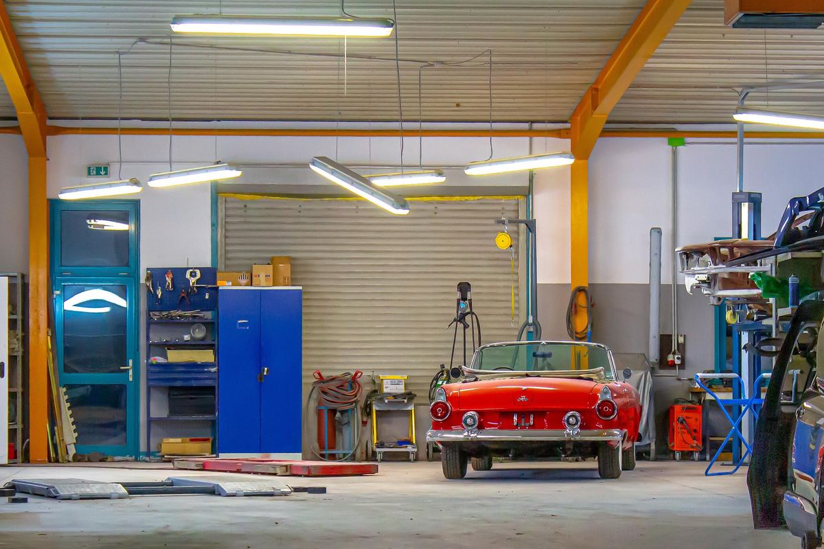 A red classic convertible in a restoration shop with a blue tool cabinet and orange steel beams